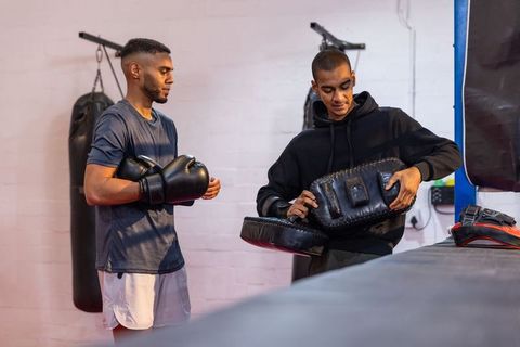 Boxing coach training young athlete with focus pads and gloves in urban gym session