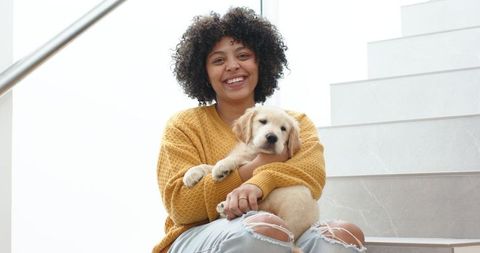 Young woman smiling while sitting on tiled stairs holding golden retriever puppy in mustard sweater