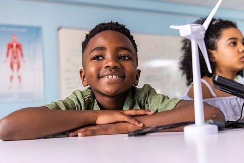 African american boy smiling while exploring wind turbine model in stem classroom