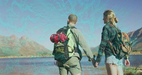 Backpacking couple holding hands at mountain lake during golden-hour outdoor adventure
