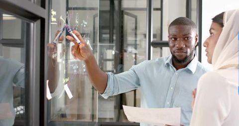 Coworkers Collaborating at Transparent Whiteboard in Modern Office