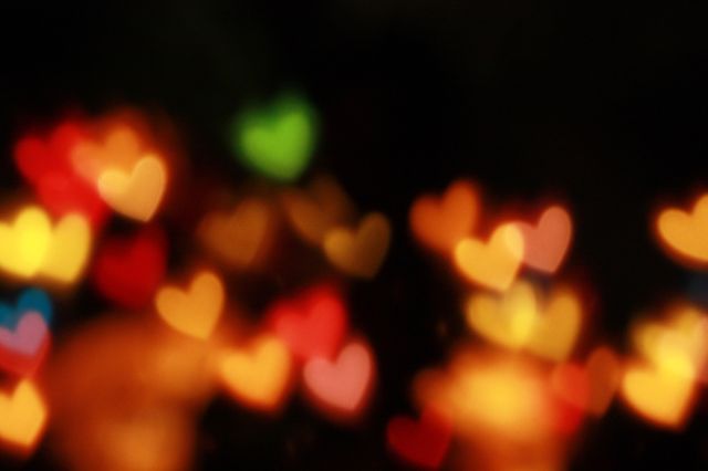 Out of focus colorful heart-shaped bokeh lights scattered on a dark background. Suitable for Valentine's Day themes, romantic designs, festive and celebratory contexts, backdrops for couples' events, and abstract art projects.