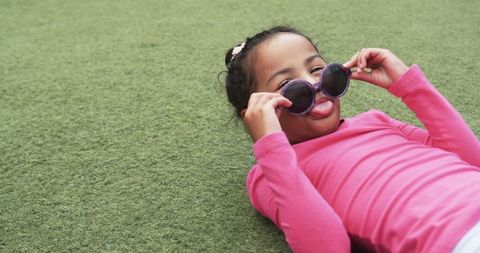 Playful young child wearing sunglasses lying on green lawn