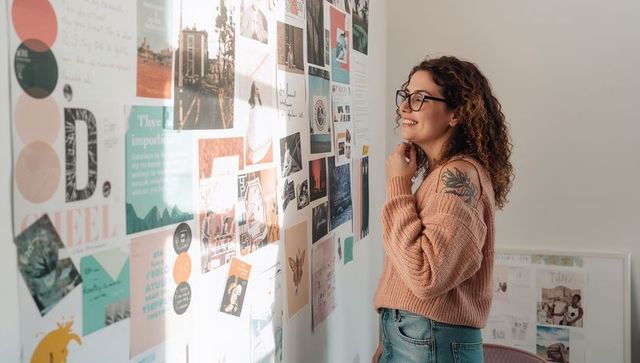 Creative professional examining moodboard in studio, smiling in peach sweater and glasses