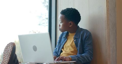 African American boy working on laptop on window seat in sunlit cozy learning nook