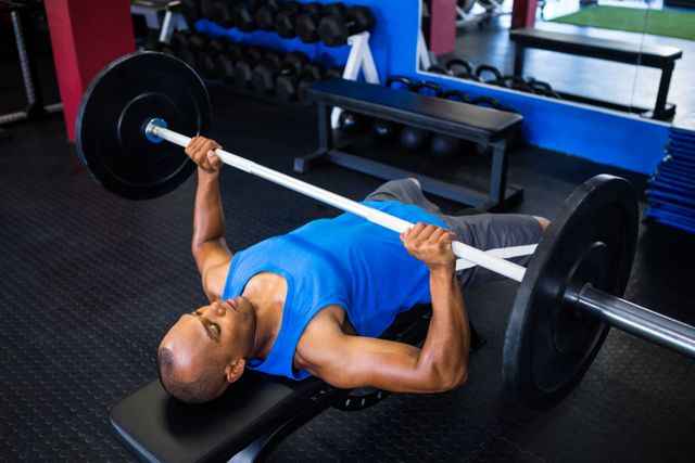 Male athlete lifting barbell while performing bench press in gym. Ideal for use in fitness blogs, workout guides, gym advertisements, and health and wellness articles.