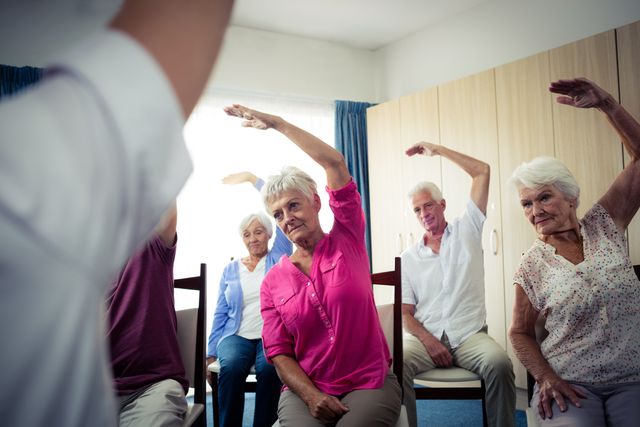 Seniors participating in a group exercise session with a nurse in a retirement home. Ideal for use in materials promoting senior health, wellness programs, retirement communities, and physical therapy services. Highlights the importance of staying active and the supportive environment in senior living facilities.