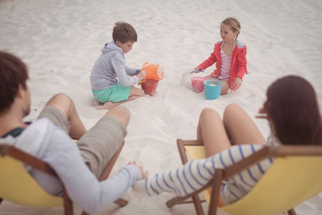 High angle view of siblings playing by parents relaxing on launge chairs at beach