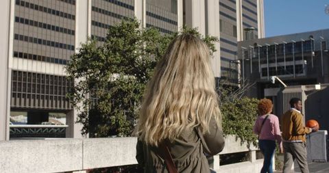 Blonde woman walking past diverse pedestrians on urban plaza with office towers