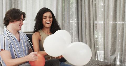 Happy Couple Blowing Balloons for Birthday Celebration at Home
