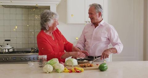 Senior couple cooking in bright minimalist kitchen preparing fresh vegetables and smiling