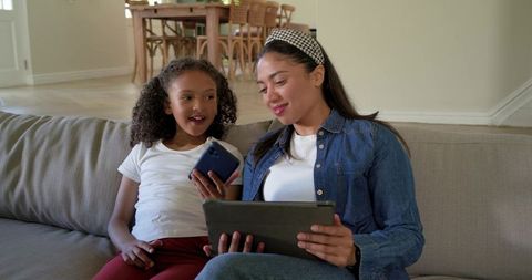 Mother and daughter using tablet and smartphone on living room couch sharing screen time