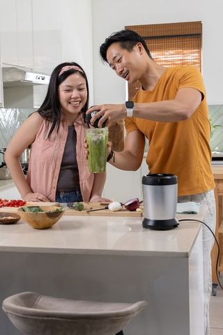 Couple preparing vibrant green smoothie at kitchen island with blender and fresh veggies