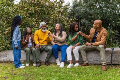 Multigenerational african american family sharing seeds on wooden bench in autumn park