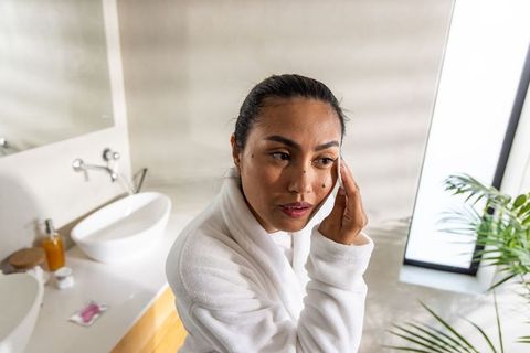 Asian woman in white robe removing makeup during morning skincare at bathroom vanity