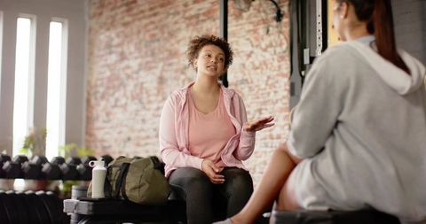 Two women chatting after workout in urban gym wearing hoodies and casual athleisure