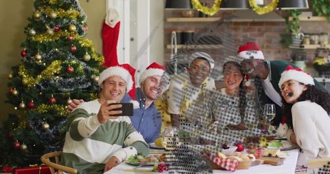 Friends wearing santa hats taking holiday selfie around festive dining table