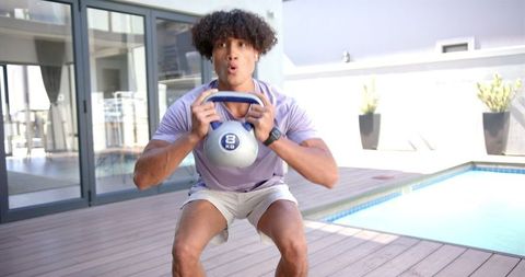 Man Exercising with Kettlebell by Poolside in Sunny Outdoor Space