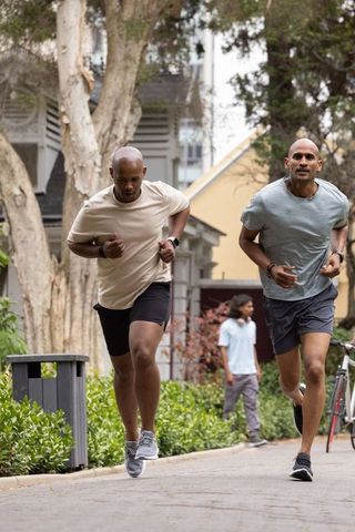African american men running side by side on neighborhood path wearing smartwatches