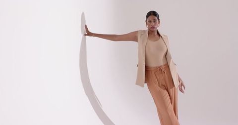 Indian Woman Leaning Against Minimalist Studio Wall Elegantly