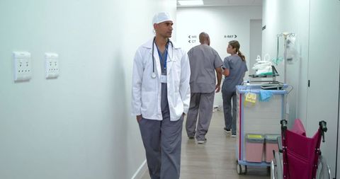 African american doctor walking hospital corridor toward mri with nurse and medical cart