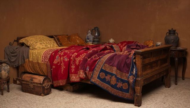 Rustic carved wooden bed with embroidered red and purple blanket and mustard pillows