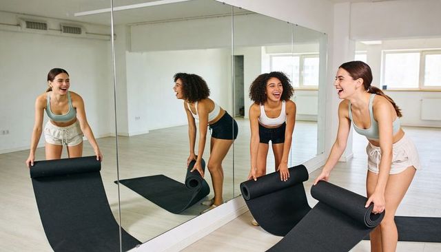 Laughing women unrolling yoga mats in bright fitness studio
