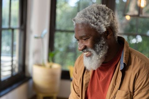 Senior african american man smiling and looking down by window, warm sunlit home portrait