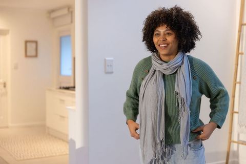 African american woman smiling in modern apartment entry wearing green sweater and gray scarf
