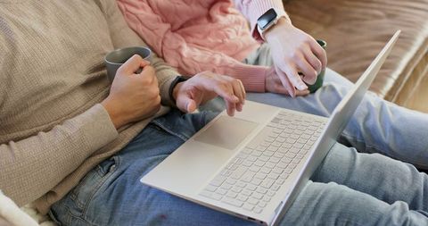 Couple browsing laptop on couch holding mugs cozy casual home comfort and connection
