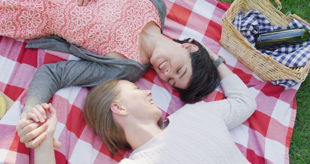 Overhead view of caucasian lesbian couple lying on the blanket in the garden during picnic. lgbt relationship and lifestyle concept