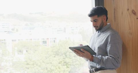 Man Using Tablet by Window in Modern Office Setting