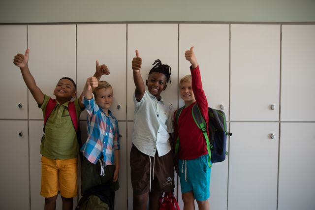 This image shows a group of happy multiracial elementary schoolboys standing in front of lockers in a school corridor, giving thumbs up. Ideal for use in educational materials, school brochures, advertisements promoting diversity and inclusion, and articles about childhood and school life.