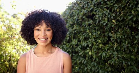 Smiling Woman with Curly Hair Posing Against Natural Green Background