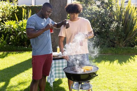Friends grilling corn in sunny backyard with charcoal grill