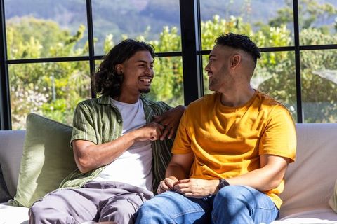 African american men laughing and talking on sunlit sofa in cozy modern living room