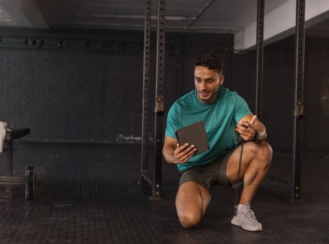 Male personal trainer kneeling timing workout using tablet and stopwatch