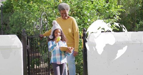 Grandmother and child harvesting apples at garden gate, sharing joyful outdoor moment