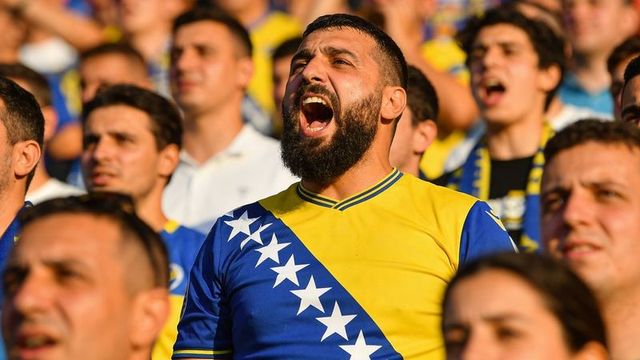 Passionate bosnian football supporter chanting in sunlit stadium crowd wearing flag jersey