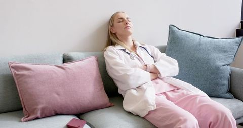 Overworked nurse resting on couch with stethoscope and smartphone, cozy minimalist break