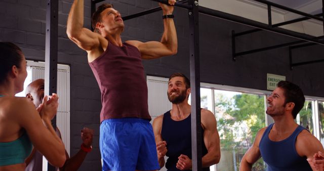 Men performing pull-up exercise while friends applauding him in gym