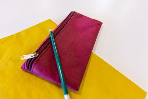 Magenta zippered pouch resting on white desk with green pencil and yellow paper
