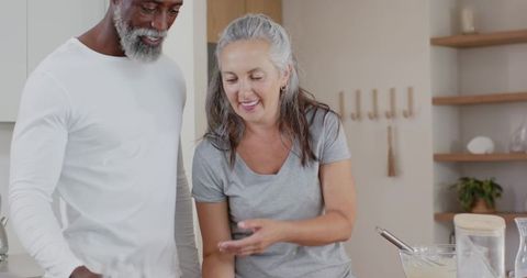 Senior couple preparing batter together in bright kitchen, sharing joyful cooking moment