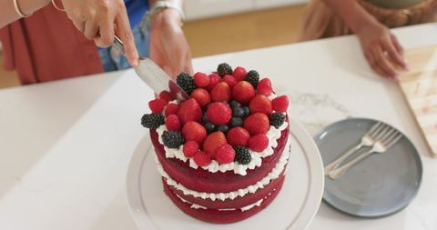 Multicultural women cutting red velvet layered cake topped with fresh mixed berries