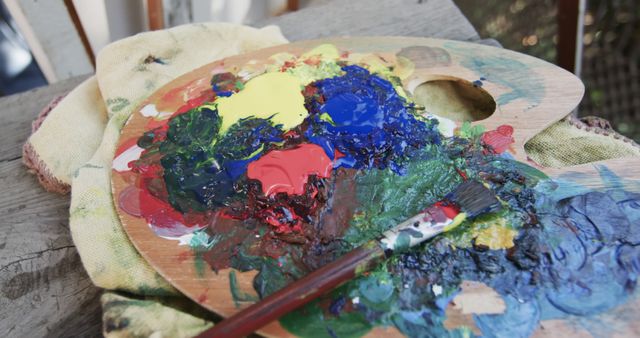 A close-up view of a paint-stained wooden artist's palette with clumps of bright acrylic paint and a paintbrush resting on it. Ideal for use in articles or advertisements related to art supplies, creative hobbies, and educational content about painting techniques.