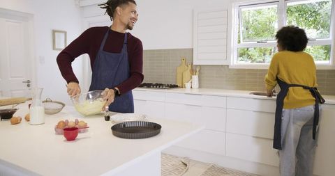 African american couple whisking batter and washing dishes in modern kitchen