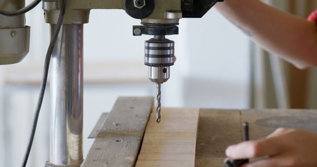 Drill press being operated at a woodworking workshop. Perfect for illustrating industrial tools, home improvement projects, DIY guides, carpentry tasks, and manufacturing processes.