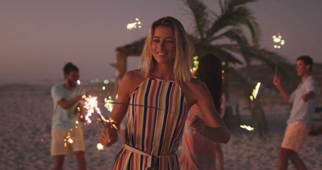 Happy caucasian woman having fun with diverse friends dancing on the beach with sparklers at sunset. Summer, free time, friendship, party, celebration and vacations.
