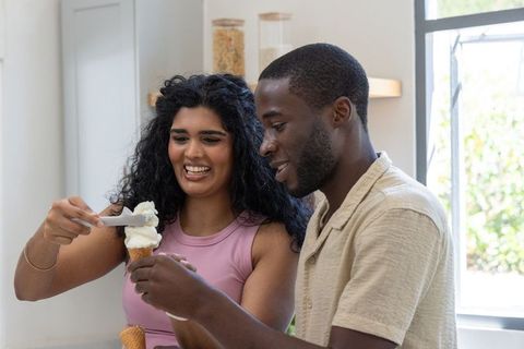 Scooping and sharing ice cream cone together in sunlit minimalist home kitchen