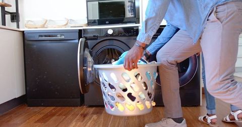 African american couple loading laundry basket into front-load washer in modern home